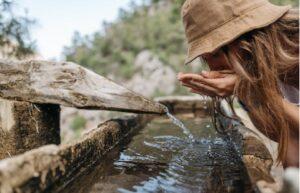 A lady drinking water closely from a natural streams
