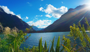 The sun shines brilliantly over a peaceful lake, with stunning mountains rising in the distance.