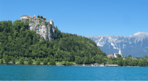A boat floats on water with a castle perched atop a mountain in the background.